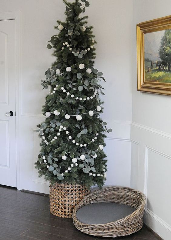 a minimal Christmas tree decorated with greenery and white pompoms only and placed into a basket looks very cool