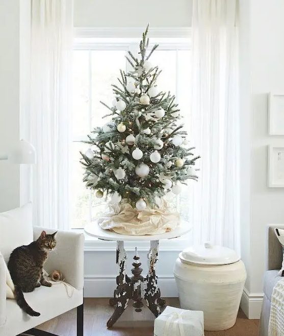 a modern snowy Christmas tree with lights, pinecones and white and gold ornaments looks beautiful and chic