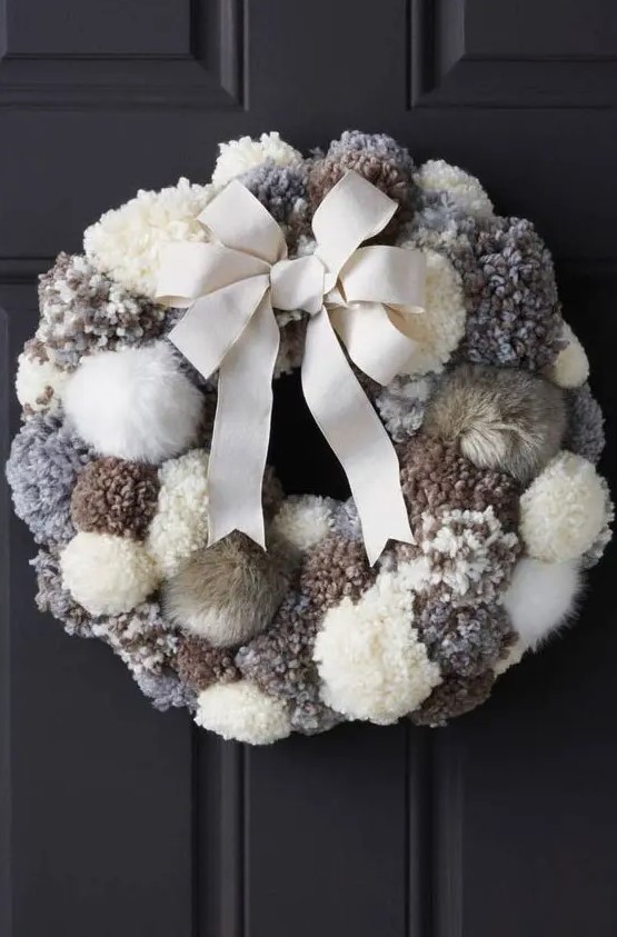 a neutral fluffy pompom wreath with a large creamy bow is a stylish and cozy decoration for your front door