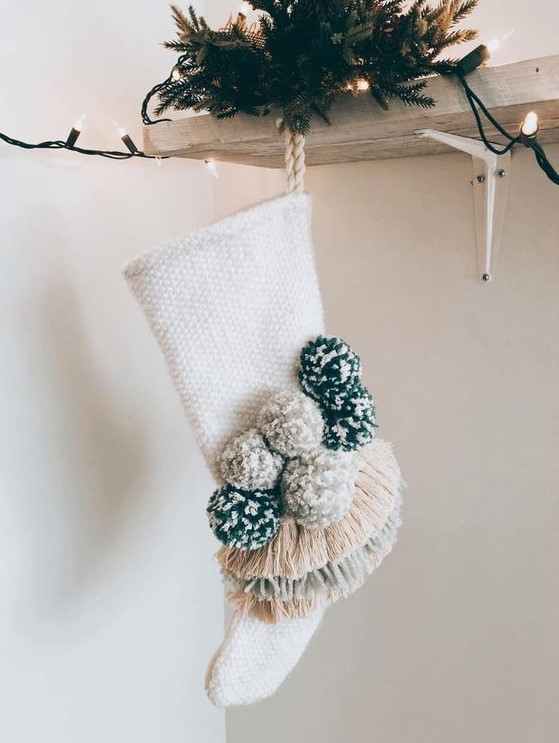 a neutral stocking with pompoms and fringe is a cool decor idea for the holidays, it will add a boho feel to your decor