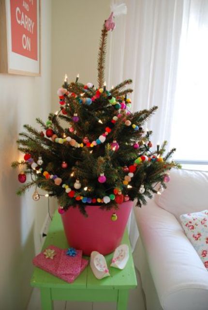 a potted Christmas tree decorated with colorful pompoms, ornaments and lights is a cool Christmas solution