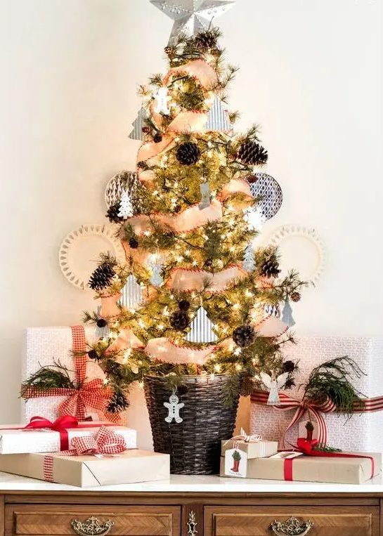 a rustic tabletop Christmas tree with lights, pinecones, little paper and clay ornaments and a basket as a base