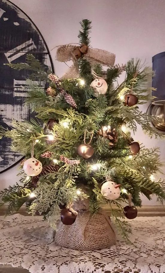 a rustic vintage tabletop Christmas tree with lights, large bells, snowman ornaments, burlap bows and garlands