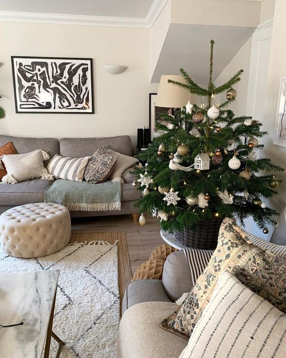 a small Christmas tree in a basket, with white and metallic ornaments, snowflakes, houses and birds