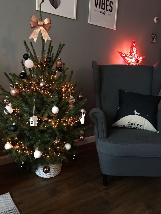 a small Christmas tree with lights, black and white ornaments, a bow on top and some houses