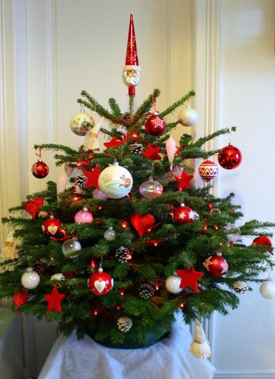 a small Christmas tree with traditional Scandi decor, with red and white ornaments, pinecones and red lights is a cool solution to try