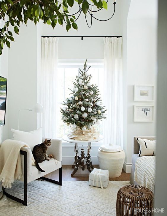 a small Christmas tree with white ornaments and lights is a cool solution for a neutral holiday space