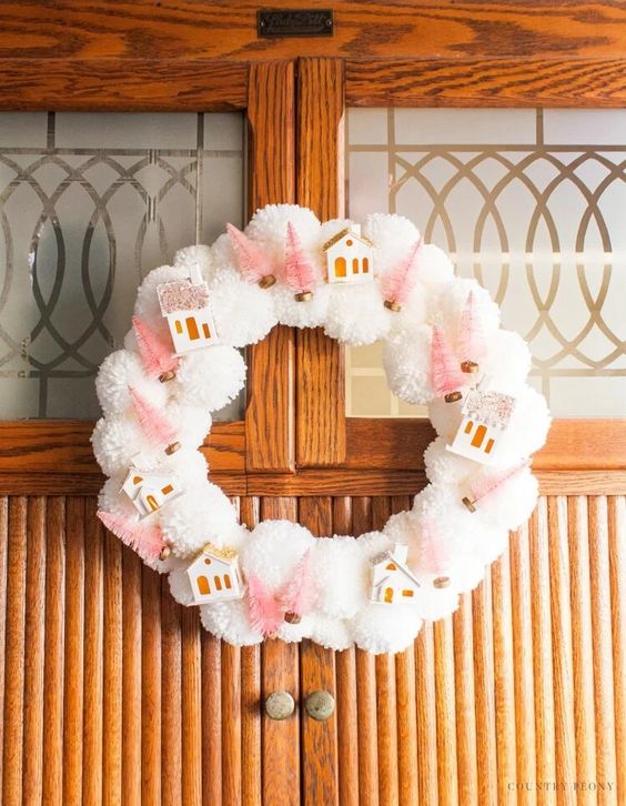 a small and cute white pompom Christmas wreath with houses and pink bottle brush trees is a cool and fun idea