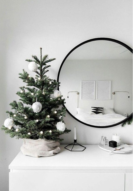 a tabletop Christmas tree with lights and white pompom ornaments is a stylish and minimal idea