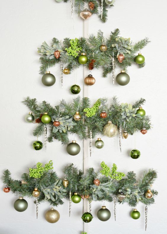 a wall Christmas tree of evergreens, berries and muted green ornaments is a chic and catchy decoration