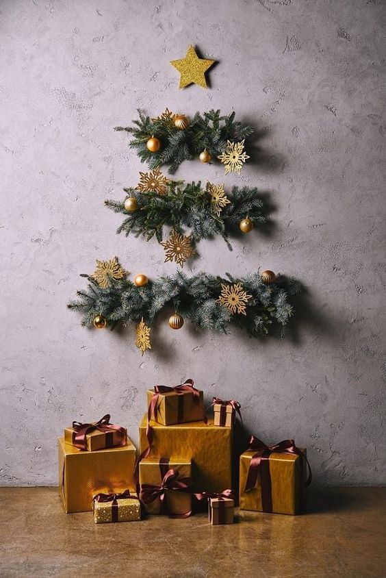 a wall Christmas tree of evergreens, gold ornaments and snowflakes and a star topper on the wall