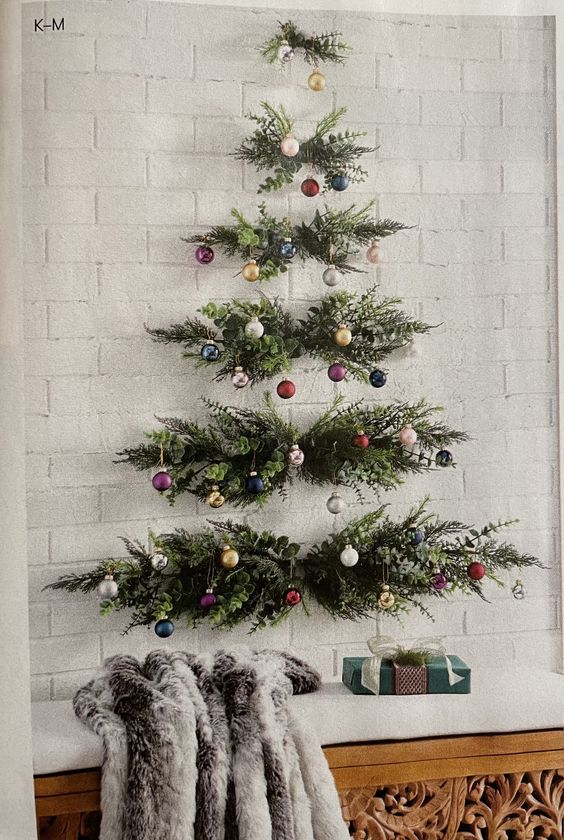 a wall-mounted Christmas tree of evergreens and greenery and colorful ornaments attached