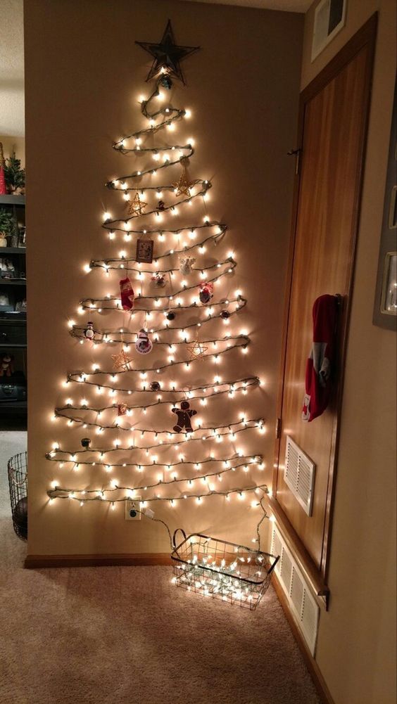 a wall-mounted Christmas tree of lights and with ornaments and decor is a cool and bold decor idea for the holidays