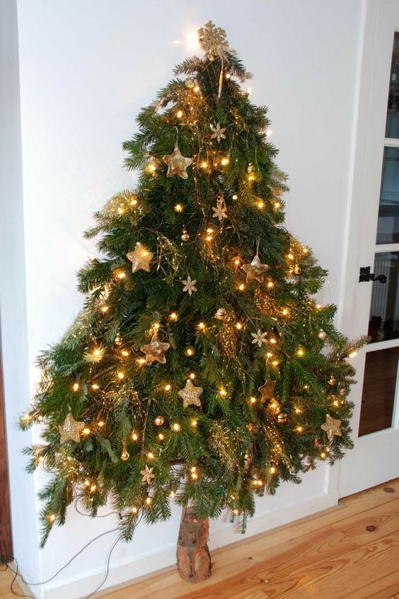 a wall-moutned Christmas tree reminding of a real one, with lights, gold ornaments and snowflakes