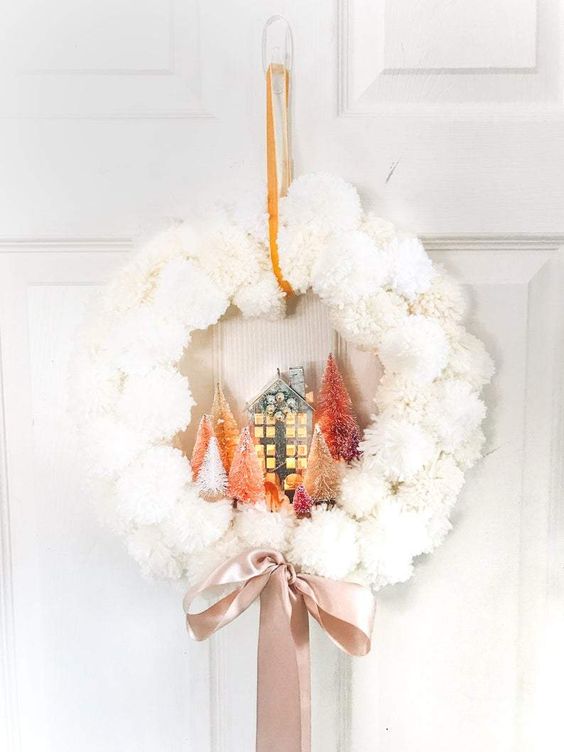 a white pompom Christmas wreath with bottle brush Christmas trees, a house and a blush silk ribbon bow