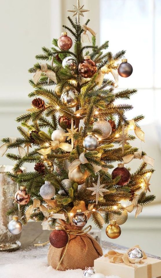an elegant tabletop Christmas tree with lights, silver, gold and brown ornaments, burlap bows and pinecones