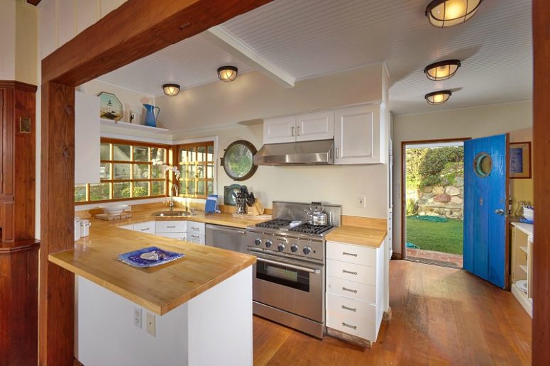 The kitchen is small, with white cabinets and a wooden beam that divides the spaces