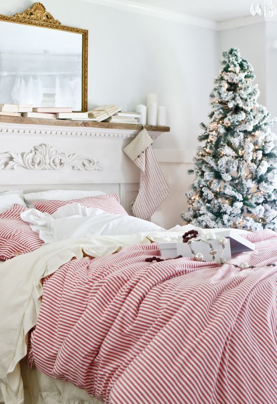a classic red and green farmhouse Christmas bedroom with striped bedding, stockings and a snowy Christmas tree
