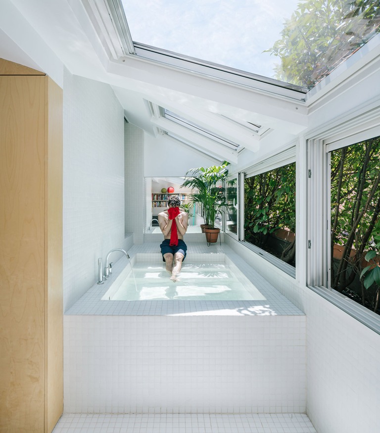 The bathtub is a large pool like space clad with white tiles, with skylights and windows that show off greenery walls The bathtub is a large pool-like space clad with white tiles, with skylights and windows that show off greenery walls