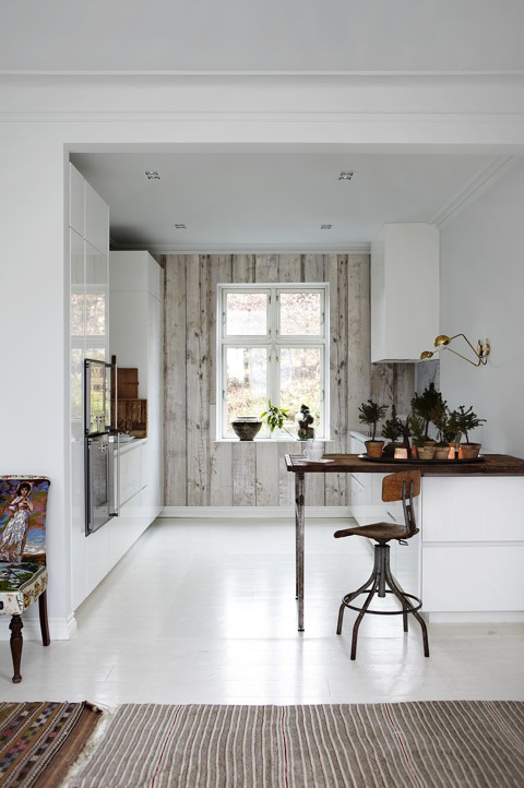The kitchen is done with sleek white cabinets, a whitewashed wood clad wall and rich colored wooden tabletops The kitchen is done with sleek white cabinets, a whitewashed wood clad wall and rich-colored wooden tabletops