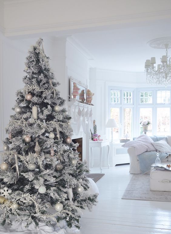 a snowy white and silver Christmas tree with various ornaments and white branch decorations