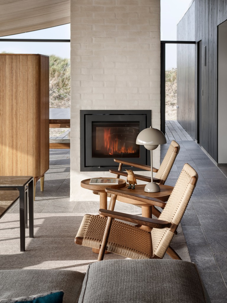 The living room features a cozy nook with a built-in fireplace, several chair and a sofa, all the materials used are natural