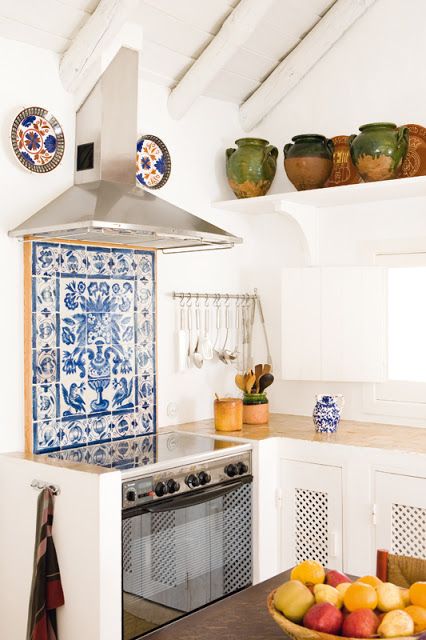 a blue mosaic tile backsplash, matching ceramics and plates on the wall and white cabinets for a Mediterranean space