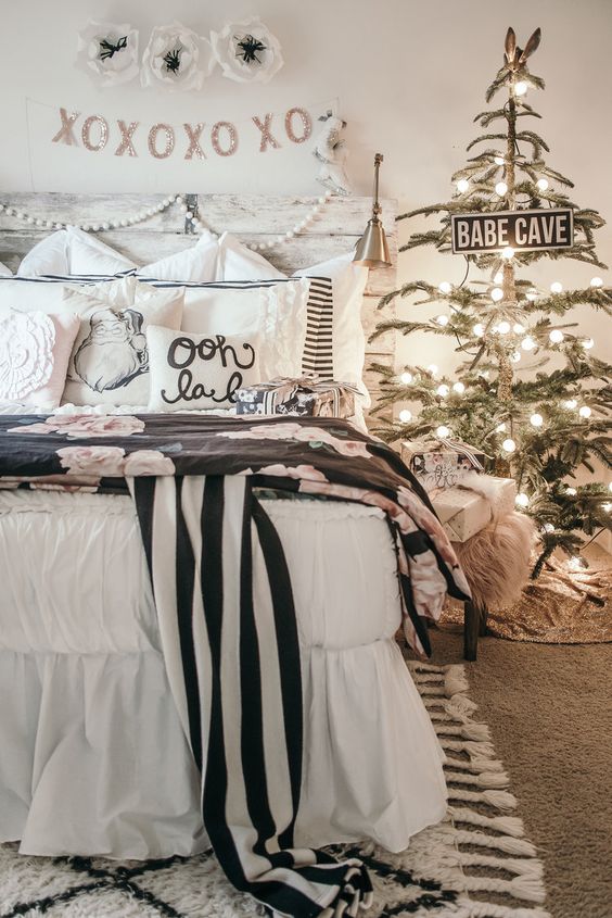 a cool festive bedroom with a Christmas tree with lights, striped and floral bedding and a pompom garland plus glitter buntings