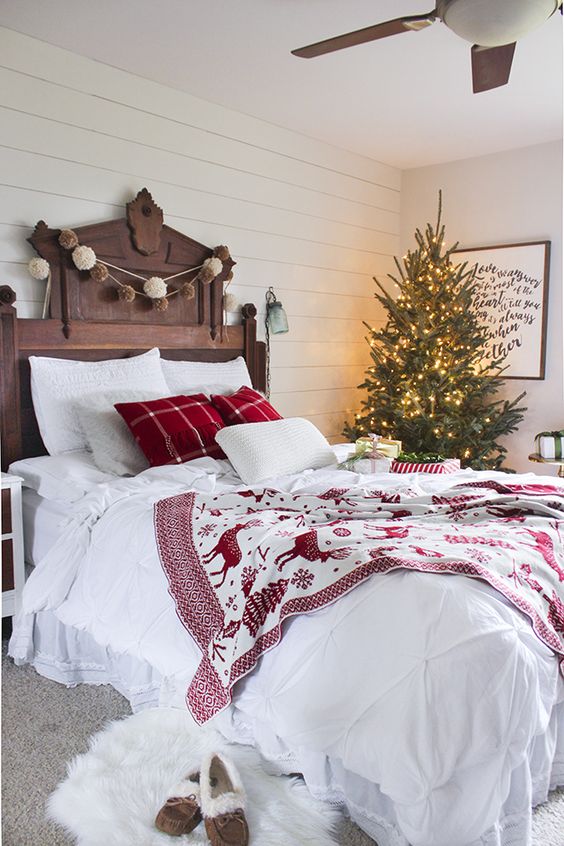 a cozy traditional bedroom with pompom garlands, a lit up Christmas tree and red and white bedding