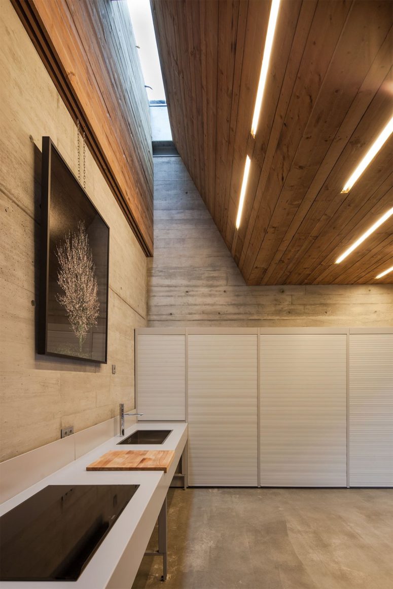 The kitchen is done with a large concrete kitchen island by the wall and closed cabinets with everythign necessary