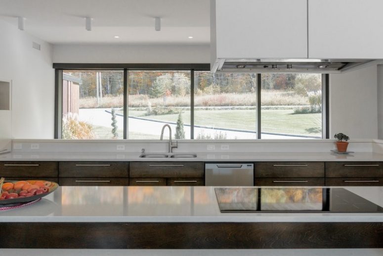 kitchen with window backsplash The kitchen is done with dark wooden cabinets and white tabletops, there's a small backsplash and a large window to catch the views
