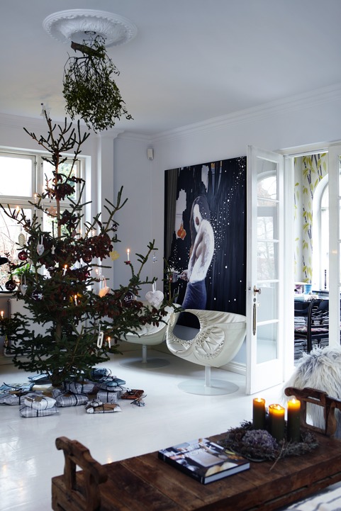The living room is done with an oversized artwork, very catchy chairs and a large Christmas tree with ornaments and hanging greenery The living room is done with an oversized artwork, very catchy chairs and a large Christmas tree with ornaments and hanging greenery