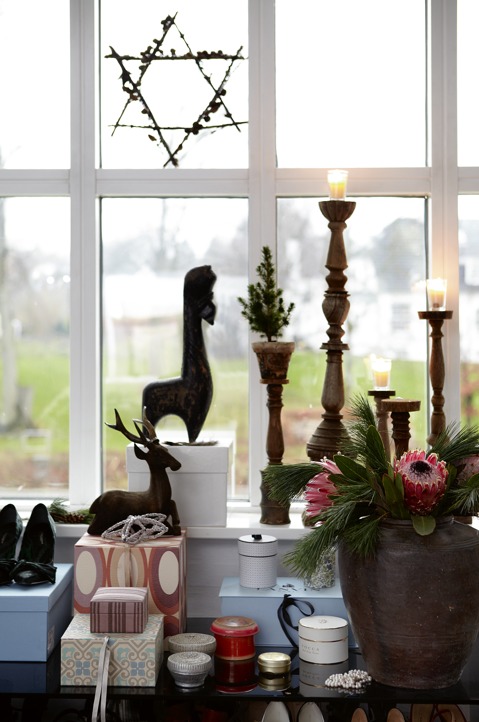 There's a windowsill display with wooden candle holders, gifts, deer figurines and lush blooms and greenery in a vase