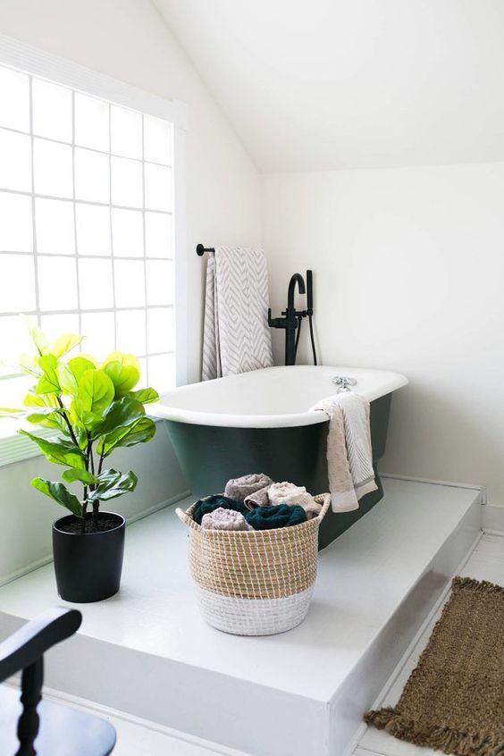 a platform bathing space with a black bathtub in the corner and a potted plant looks very cozy and comfy a platform bathing space with a black bathtub in the corner and a potted plant looks very cozy and comfy