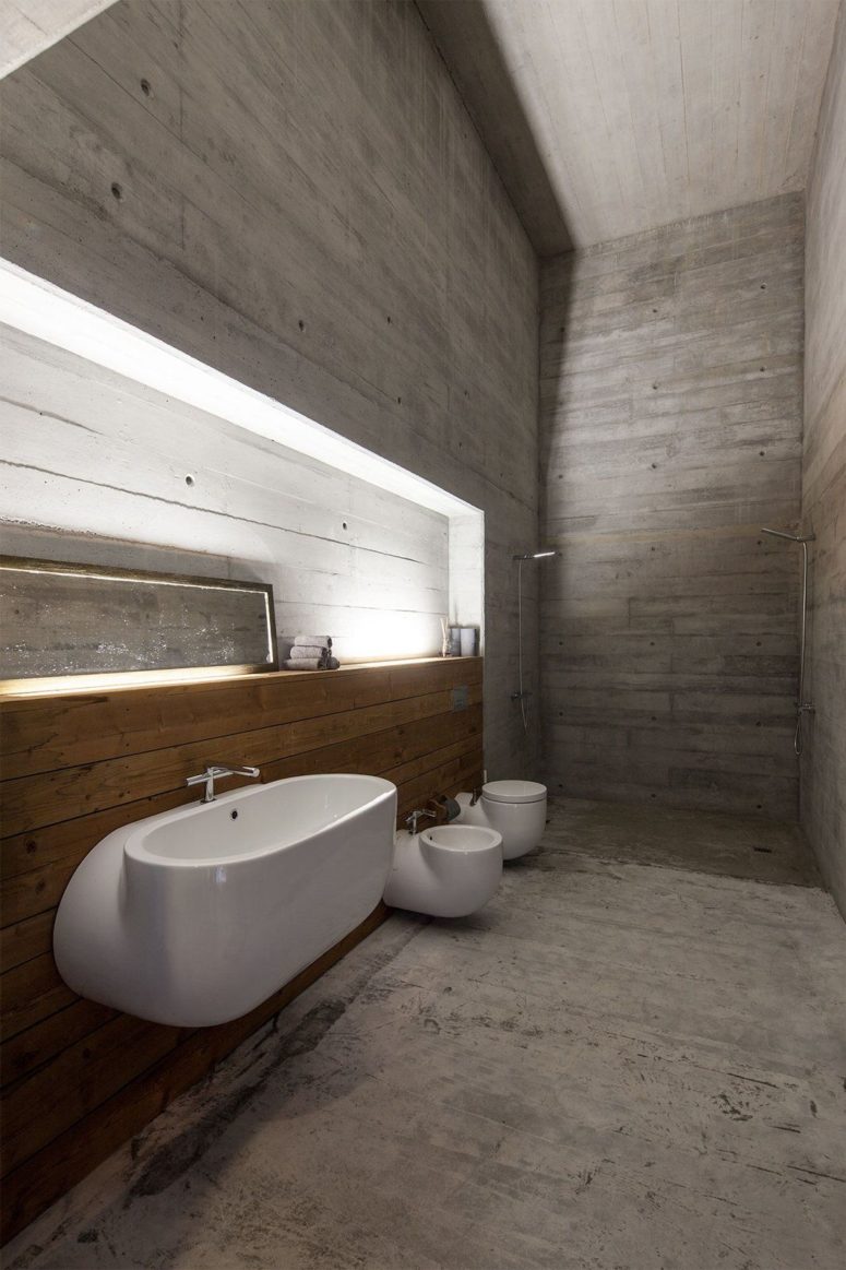 The bathroom is very spacious, it's done with concrete and wood and there's a shower in the corner
