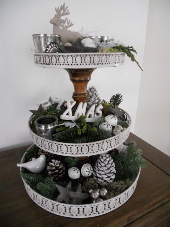 a Christmas etagere with evergreens, pincones, jingle bells, candle holders and letters