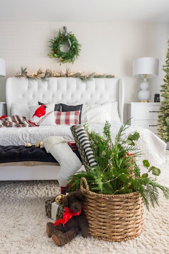 a welcoming modern Christmas bedroom with an evergreen wreath, garland, a basket with evergreens, lights and ornaments