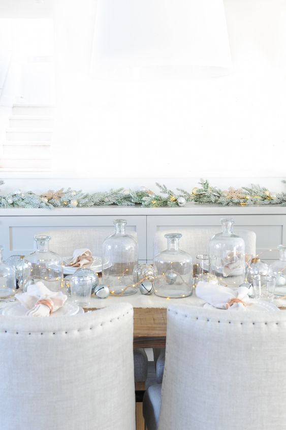 a white and silver Christmas tablescape with LEDs, jingle bells, white napkins and large bottles as vases