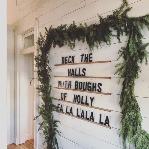 a sign made using ledges on the wall and a lush evergreen garland covering them for modern vibes