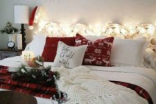 17 create a welcoming space with lights, printed and knit pillows, a white blanket, a sign over the bed decorated with pinecones and evergreens