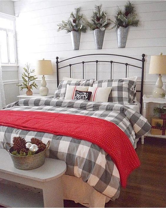 a farmhouse sleeping space with plaid, chunky knit, a trio of flocked Christmas arrangements over the bed and a display with pinecones and ornaments