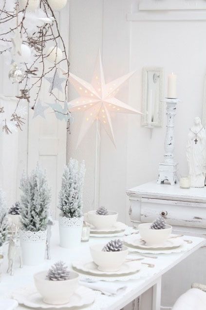 a white Christmas tablescape with snowy potted trees, stars around and whitewashed pinecones in bowls