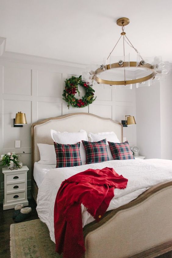 a traditional Christmas bedroom with an evergreen and red bloom wreath, plaid pillows and a red blanket