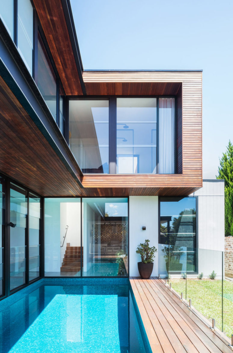 This small backyard with a a narrow pool and a deck is covered with a glass fence