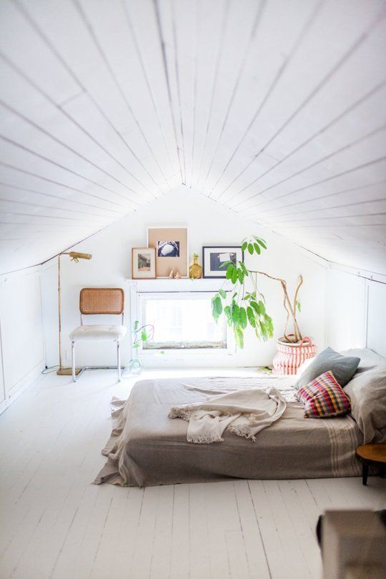 an all-white attic bedroom with neutral wood and textiles, with potted greenery and artworks