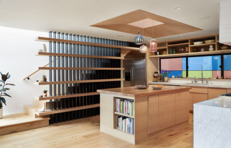 The kitchen is done with light-colored wooden cabinets, a colorful tile backsplash and hanging lamps over the kitchen island