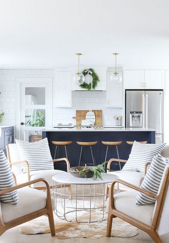 a white kitchen with a navy kitchen island with wooden touches and stone countertops for a beach home