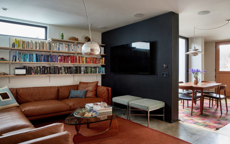 A small living room is done with leather furniture, open shelving and a cool glass coffee table