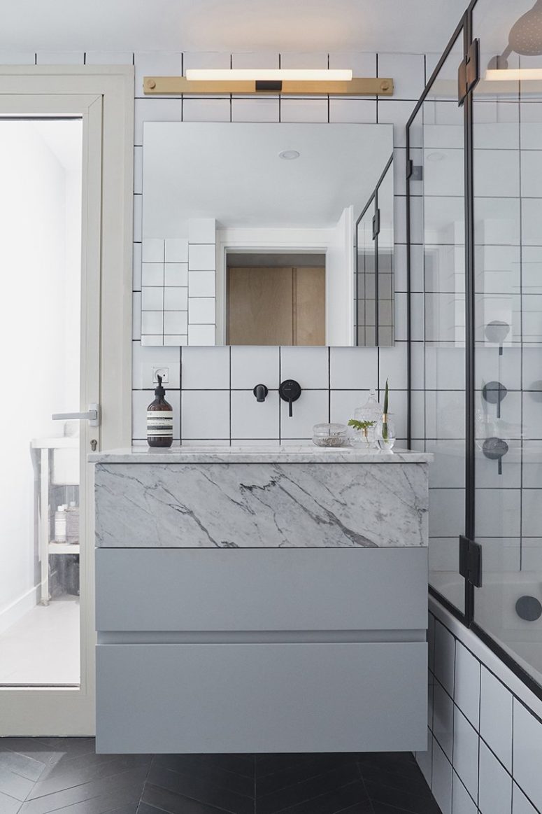 One bathroom is done with white tiles and black grout plus marble and wooden touches