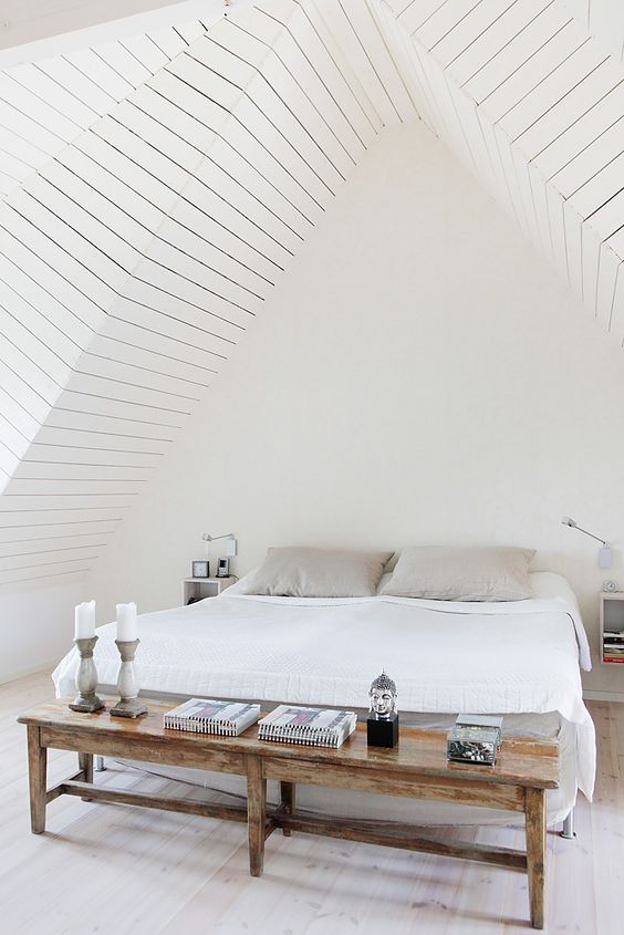 an attic bedroom done in creamy shades, with a neutral wooden floor, various neutrals to style the bed